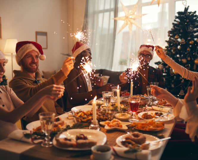 five people sitting around a festive table in santa hats with sparklers lit.