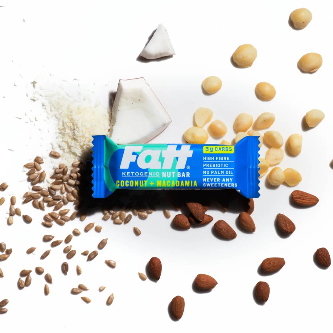 Fatt - Coconut + Macadamia 2 Fatt - Coconut + Macadamia bar on a white background with coconut, almonds and macadamia nuts spread out behind it.
