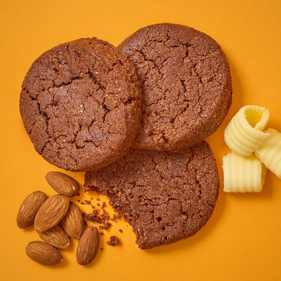 Keto Cookies - Choc - 1080 - V3 three keto choc cookies on an orange background with almonds and butter