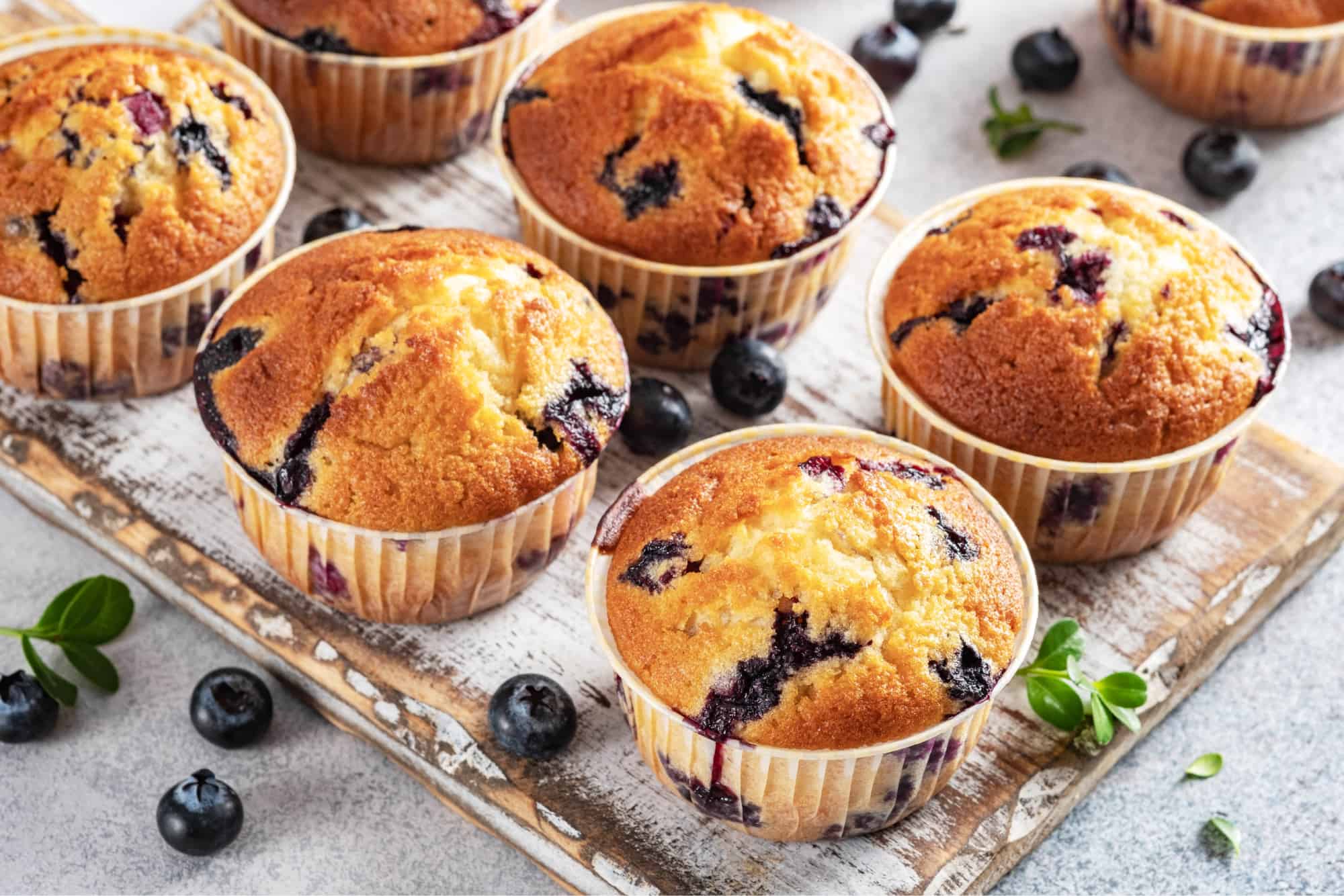 6 Low-carb blueberry muffins on a tray with blueberries scattered around