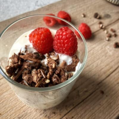 Raw Gorilla Peanut Butter and Chocolate Granola in a glass with almond milk and raspberries, shot from above.
