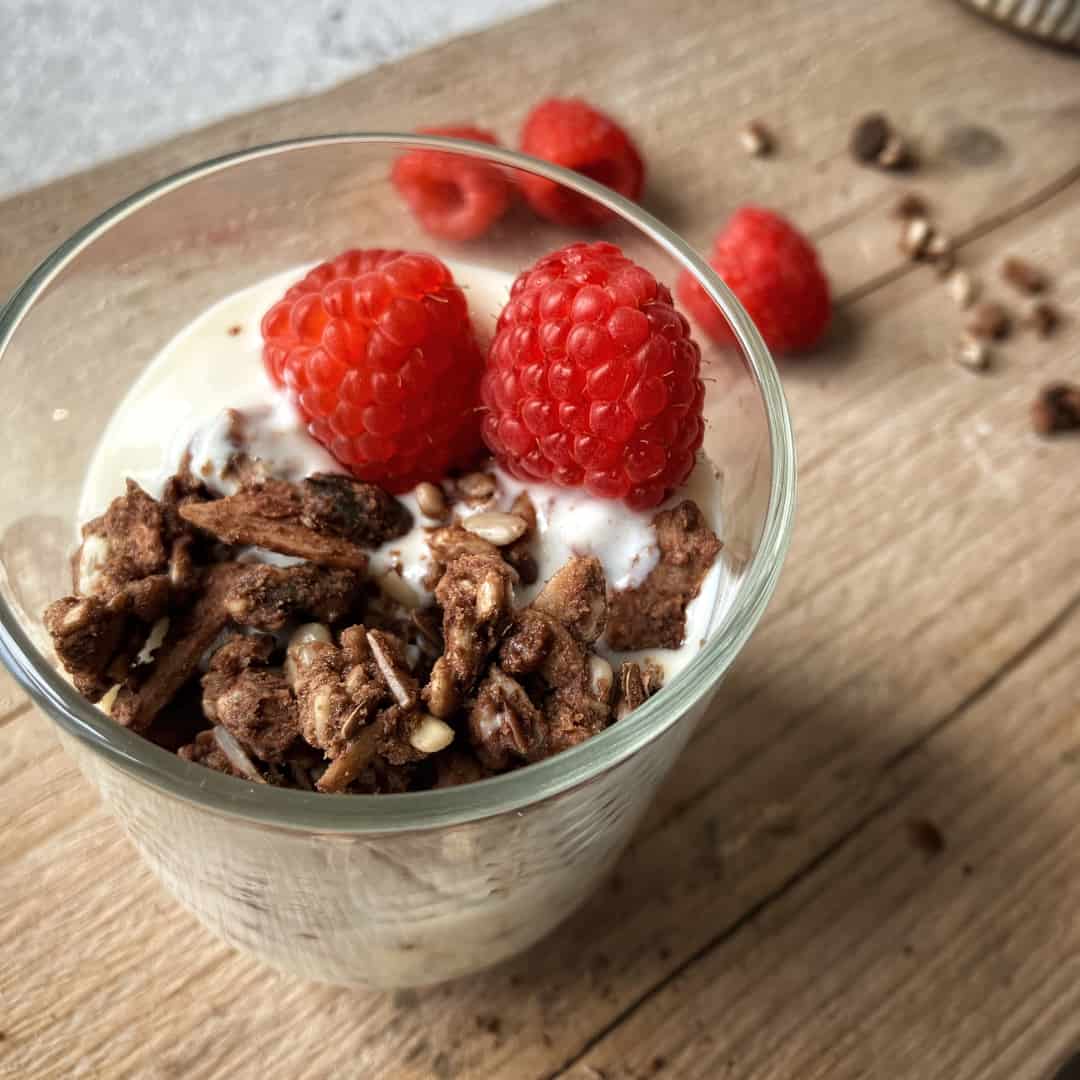 Raw Gorilla Peanut Butter and Chocolate Granola 3 Raw Gorilla Peanut Butter and Chocolate Granola in a glass with almond milk and raspberries, shot from above.