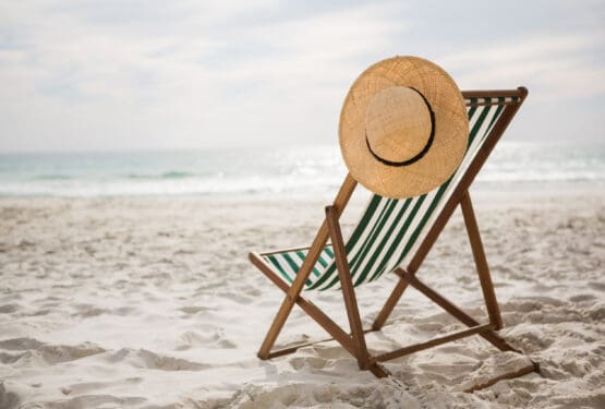 a beach char on a sandy beach with a sun hat resting on the top.