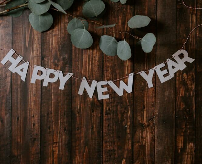 happy new year banner on a brown wooden wall with eucalyptus branches